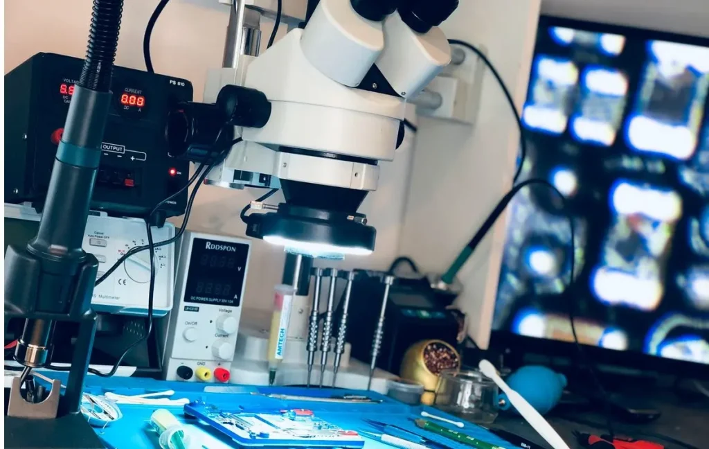Tehnician executând microsudură sub microscop pe placa de bază a unui telefon